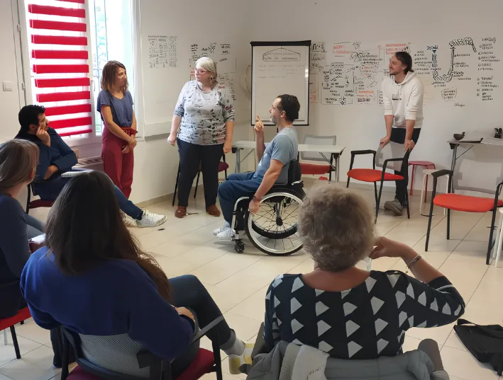 Atelier Théâtre Forum Han1Pro en entreprise : collaborateurs assis en cercle autour d'une scène rejouée, dont un participant en fauteuil roulant
